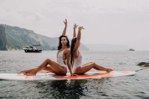 Woman sup yoga. Middle age sporty woman practising yoga pilates on paddle sup surfboard. Female stretching doing workout on sea water. Modern individual hipster outdoor summer sport activity