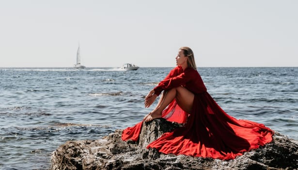 Woman travel sea. Young Happy woman in a long red dress posing on a beach near the sea on background of volcanic rocks, like in Iceland, sharing travel adventure journey