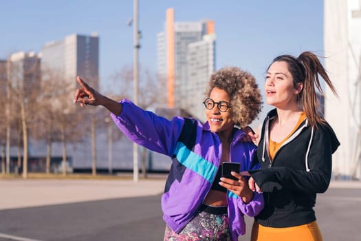 two female runners pointing ahead standing in the city ready to run, concept of friendship and sportive lifestyle