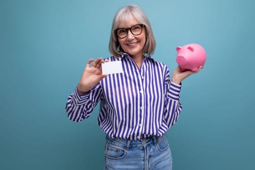 pension contribution. middle-aged woman with gray hair holding a piggy bank and a credit card for retirement on a bright studio background.