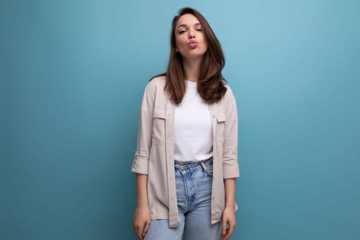 charming young dark-haired lady in informal clothes sends a kiss on a blue background.