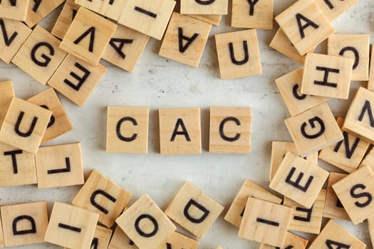 Top down view, pile of square wooden blocks with letters CAC (stands for Customer acquisition cost) on white board. 