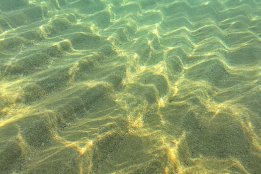 Underwater photo, sun shines to sand "dunes" on sea floor in shallow water near beach - abstract marine background.