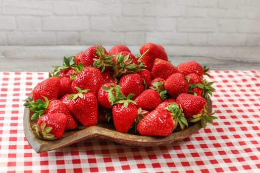 Wooden carved bowl with strawberries, red gingham pattern tablecloth under it.