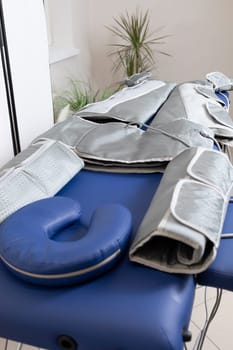 Pressure therapy gray massaging suit on blue couch in spa, treatment of varicose veins, edema, lymphatic drainage, weight loss. Relaxation, pressotherapy machine,device. No people. Vertical,copyspace