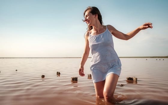 Young woman walking in red lake. Happy girl in striped white dress smiling and looking away. Sexy fashion woman enjoys summer holidays. download photo