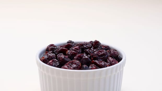 Closeup Superfood Heap Of Dried Cranberries In White Bowl On Beige Background. Selective Focus. Sweet Dehydrated Cranberries. Nutrients And Vitamins. Horizontal Plane. High quality photo