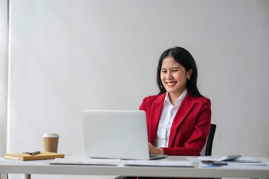 Cheerful business lady working on laptop in office, Asian happy beautiful businesswoman in formal suit work in workplace. Attractive female employee office worker smile...