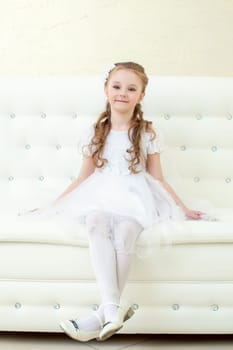 Funny little girl posing sitting on white sofa, close-up