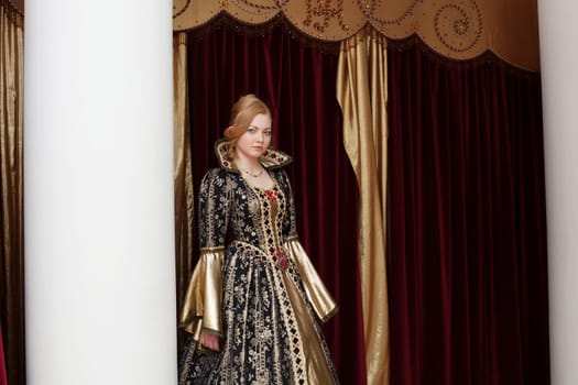 Young actress in royal dress posing on curtain backdrop