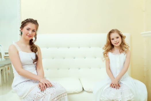 Image of lovely elegant sisters sitting on white couch