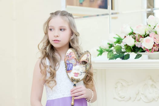 Shy little girl posing with masquerade mask, close-up