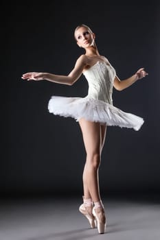 Image of cute young ballerina dancing in studio, on gray background