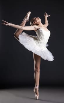 Image of flexible cute ballerina dancing in studio, on gray background