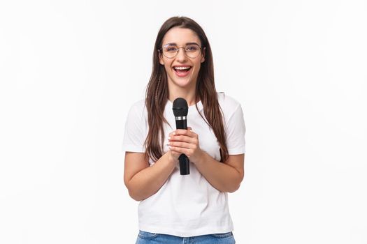 Portrait of cute and happy young caucasian woman having fun, spending self-isolation or leisure time singing karaoke, holding microphone, perform with favorite song, smiling enthusiastic.