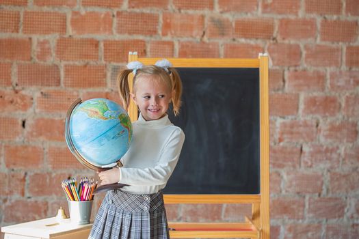 Portrait of caucasian schoolgirl standing in front of chalkboard with globe in her hands, back to school concept