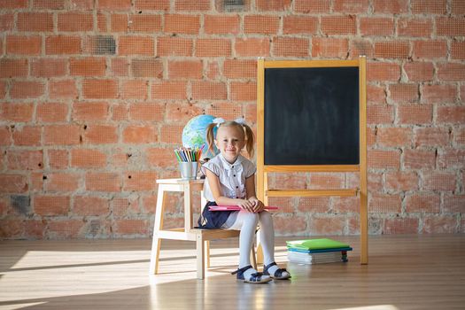 Portrait of caucasian school kindergarten girl sitting in front of blackboard with a book, back to school concept