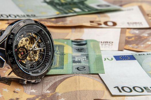 Time is money.A beautiful mechanical watch in close-up lies on the euro money.Manual counting of euro banknotes.Cash euro bills.The history of cash in Europe.European banknotes are a tangential policy