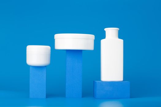 Trendy futuristic composition in blue colors with set of cosmetic bottles with beauty products on geometric props against blue background. Concept of anti acne or regular basic skin treatment