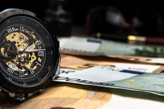 Time is money.A beautiful mechanical watch in close-up lies on the euro money.Manual counting of euro banknotes.Cash euro bills.The history of cash in Europe.European banknotes are a tangential policy