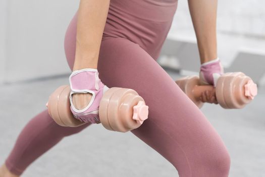 No face visible. Girl in a tight pink outfit working out with dumbbells. Beautiful fitness girl training legs and lifting weights. Girl doing sports in a loft interior studio. Sport concept.