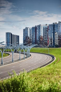 Empty expressway of the western high-speed diameter in st. petersburg in clear sunny weather, green lawns along the road, new residential buildings stand on a hillock, lamppost, colourful facade. High quality photo