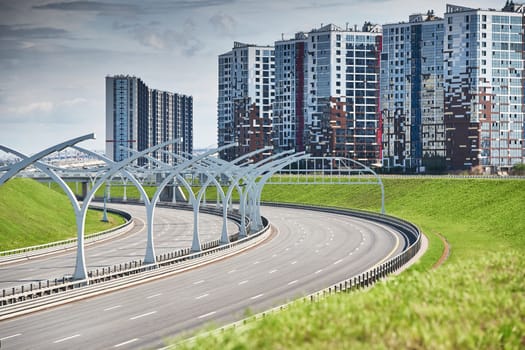 Empty expressway of the western high-speed diameter in st. petersburg in clear sunny weather, green lawns along the road, new residential buildings stand on a hillock, lamppost, colourful facade. High quality photo