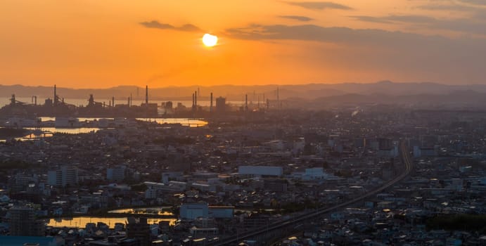 Orange sun in hazy sky over refinery smokestacks by industrial city. High quality photo