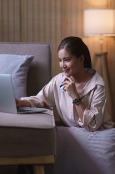 Pretty asian woman shopping online with credit card and smartphone while sitting on sofa at home.