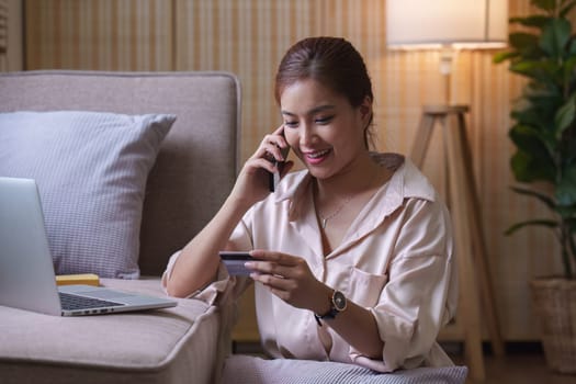 Pretty asian woman shopping online with credit card and smartphone while sitting on sofa at home.