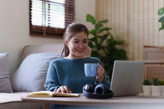 Young asian relaxed smiling pretty woman relaxing with laptop at home. Female feeling joy enjoying with mobile phone on cozy couch.