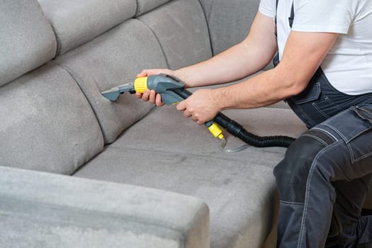 Dry cleaner's man employee removing dirt from furniture in flat, closeup, vacuum clean sofa with professional equipment. cleaning sofa with washing suction cleaner closeup.
