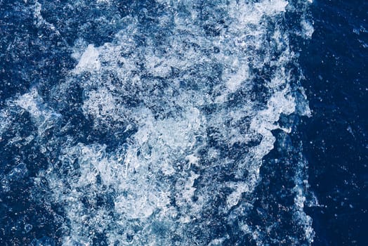 Abstract blue sea water with white waves. Blue sea texture with waves and foam. Rough deep turquoise and blue Mediterranean sea. Sea water top view.