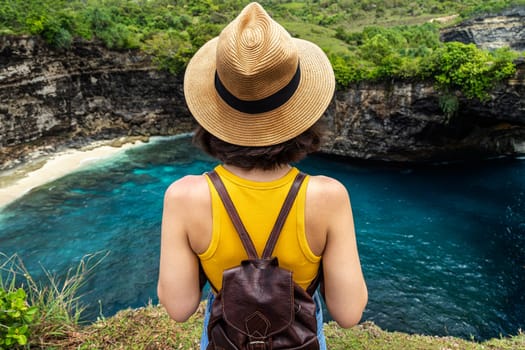 Rear view of young woman traveler standing on cliff looking at Broken Beach Nusa Penida Bali. Summer vacation. Traveling, freedom and wellness concept.