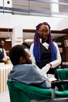 African American man guest holding phone near nfc terminal making contactless mobile payment in hotel. Tourist paying for services with smartphone via pos machine while waiting for check-in at resort