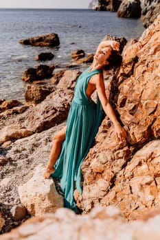 Woman green dress sea. Woman in a long mint dress posing on a beach with rocks on sunny day. Girl on the nature on blue sky background