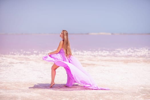 Woman pink salt lake. Against the backdrop of a pink salt lake, a woman in a long pink dress takes a leisurely stroll along the white, salty shore, capturing a wanderlust moment