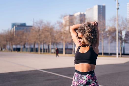 smiling african american fit woman stretching arms in an urban park, concept of health and sportive lifestyle