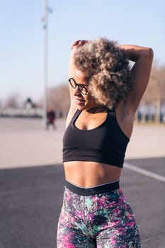 vertical photo of a smiling african american fit woman stretching arms in an urban park, concept of health and sportive lifestyle