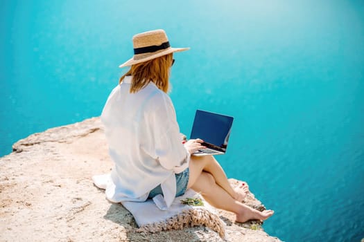 Freelance woman working on a laptop by the sea, typing away on the keyboard while enjoying the beautiful view, highlighting the idea of remote work