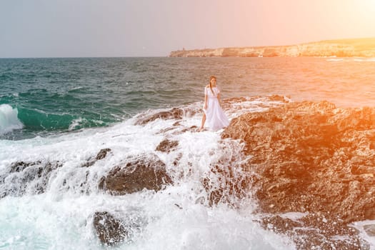 A woman stands on a rock in the sea during a storm. Dressed in a white long dress, the waves break on the rocks and white spray rises