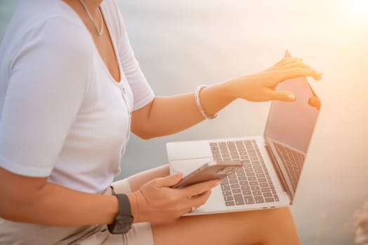 Freelance close up woman hands writing on computer. Well looking middle aged woman typing on laptop keyboard outdoors with beautiful sea view