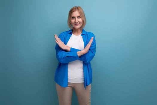 portrait of a middle-aged blond woman in a casual stylish shirt with crossed arms on a blue background with copy space.