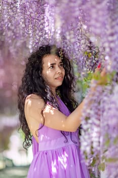 Woman wisteria lilac dress. Thoughtful happy mature woman in purple dress surrounded by chinese wisteria.