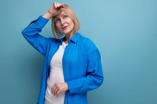 pensive adult woman with blond hair dreaming on blue background with copy space.