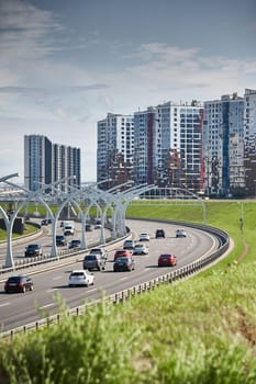 Russia, St.Petersburg, 07 July 2023: Expressway of the western high-speed diameter in clear sunny weather, green lawns along the road, new colourful residential buildings stand on a hillock, lamppost. High quality photo