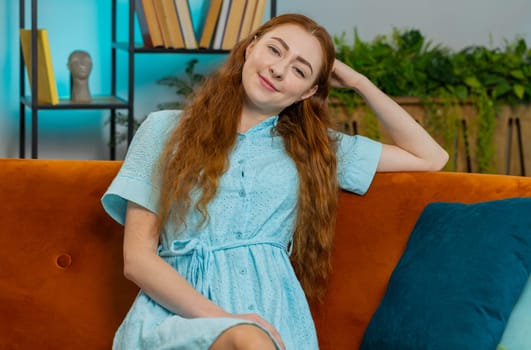 Portrait of happy calm young redhead woman at home couch smiling friendly glad expression looking away dreaming resting, relaxation feel satisfied concept good news, celebrate win. Girl in living room