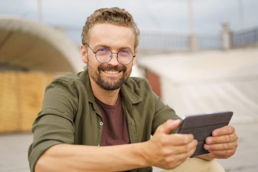 Man sitting on stairs outdoors, wearing charming smile as reads good news. With expression of pure joy and contentment, radiates positivity and happiness. . High quality photo