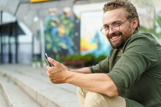 Man sitting on stone stairs on street, using pocket PC. With compact and portable device in hand, he effortlessly combines technology with surroundings. urban backdrop adds modern touch to scene. High quality photo
