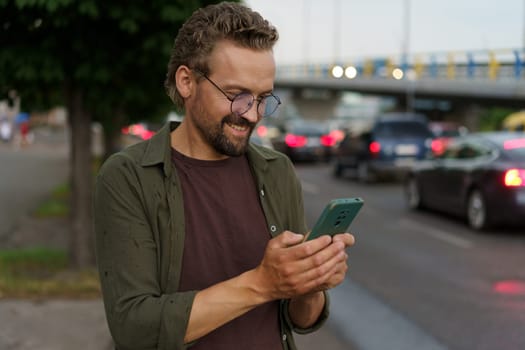 Man using phone on evening city street, presumably to call taxi cab driver. soft evening lighting adds touch of ambiance to urban environment. Convenience and technology that enables ride-hailing services. . High quality photo